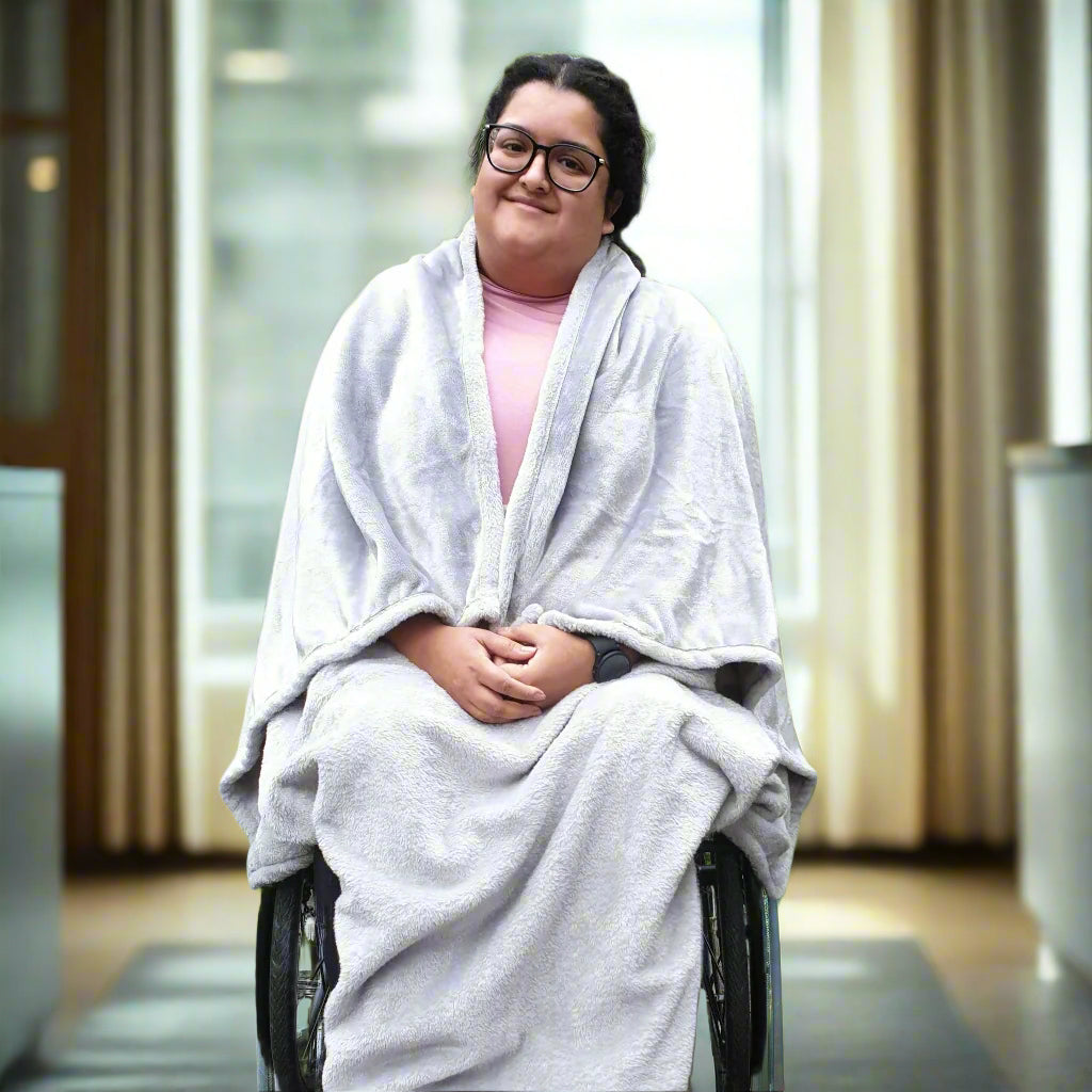 Woman sitting in a wheelchair wearing a Snhug Sit sitting blanket indoors, showing warmth, comfort, and inclusive seated design.