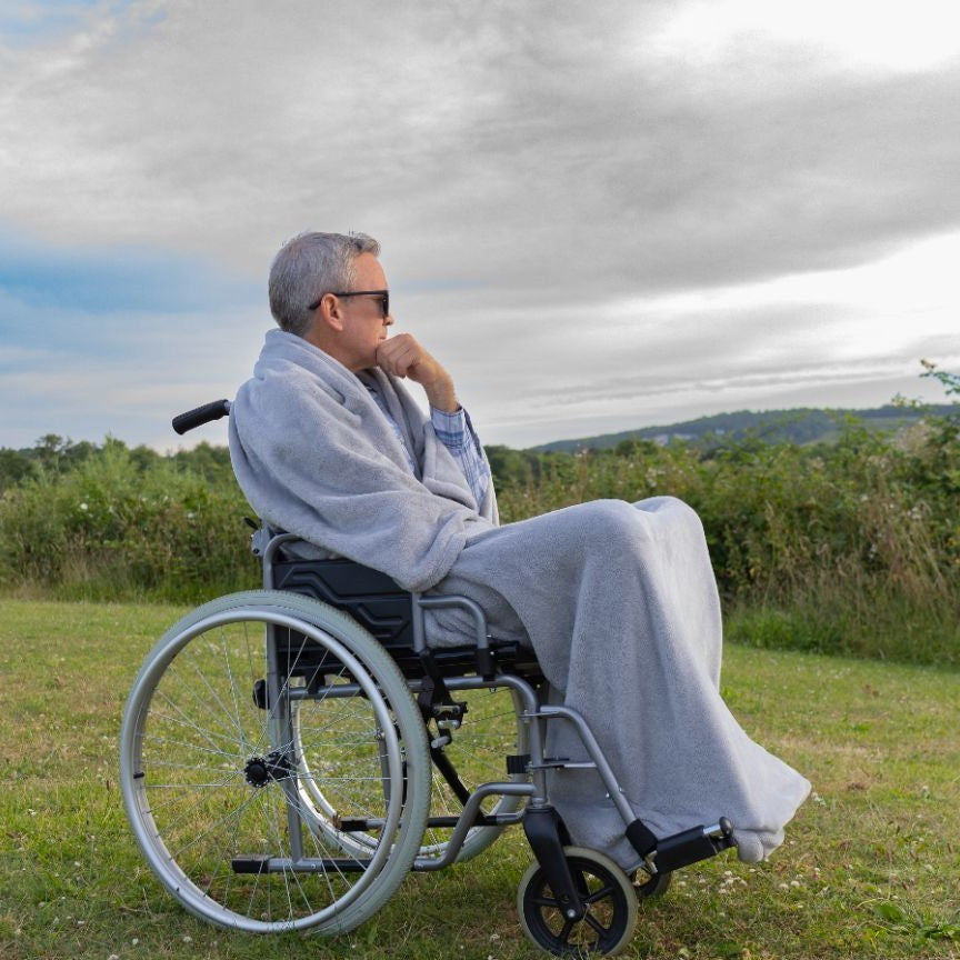 Man outdoors in a wheelchair wearing a Snhug Sit sitting blanket, staying warm and comfortable while enjoying nature.