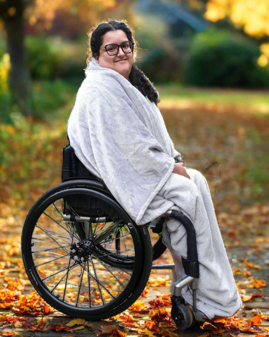 Woman outdoors in a wheelchair wearing a Snhug Sit sitting blanket, staying warm and comfortable while enjoying fresh air in autumn.


