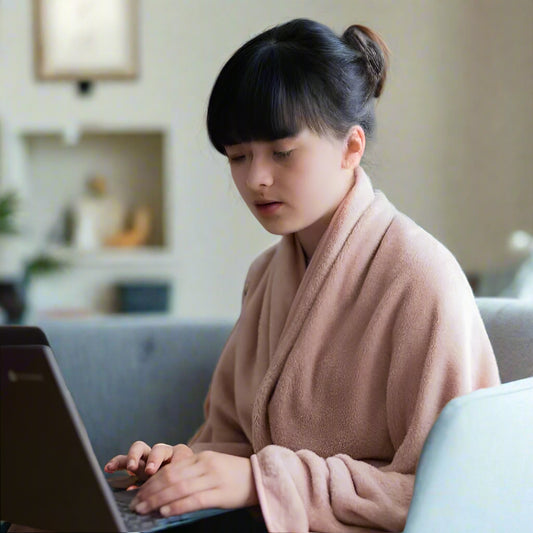 Woman seated at home wearing a Snhug Sit sitting blanket while using a laptop, demonstrating comfortable warmth and ease for remote work or study.



